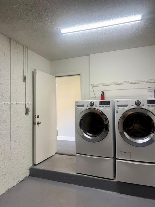 Laundry area featuring white front-load washer and dryer on pedestals, overhead wire shelving, textured wall finish, and painted concrete flooring