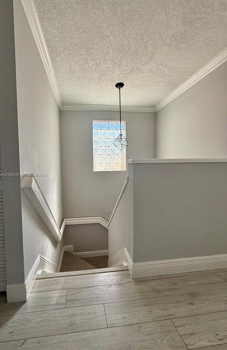 Wood-finish flooring, crown molding, glass block window, and geometric pendant lighting
