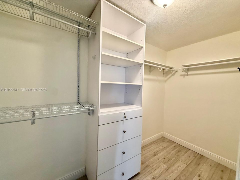 Walk-in closet featuring white built-in shelving, a four-drawer storage unit, metal wire hanging racks, and wood-finish flooring