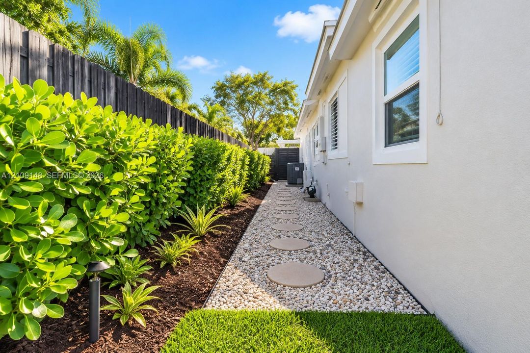 Side yard featuring a stone pathway, privacy fencing, manicured hedges, and professional landscape beds with mulch