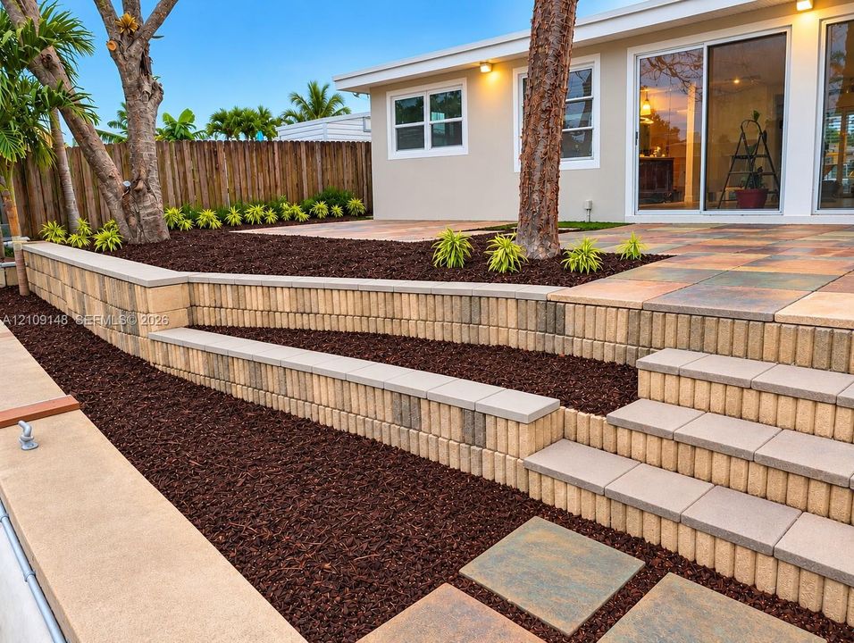Terraced backyard featuring multi-level retaining walls, integrated staircases, large-format paver patio, wood-finish privacy fencing, and mulched landscaping beds