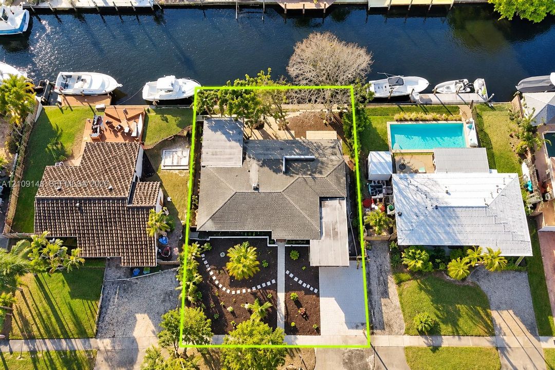 Waterfront property featuring a private bulkhead, canal access, a concrete driveway, and landscape beds with mature palm trees