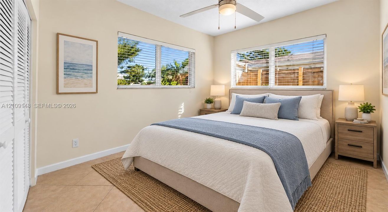 Neutral-toned walls, tile flooring, dual windows with horizontal blinds, built-in louvered closet doors, and ceiling fan with integrated light fixture