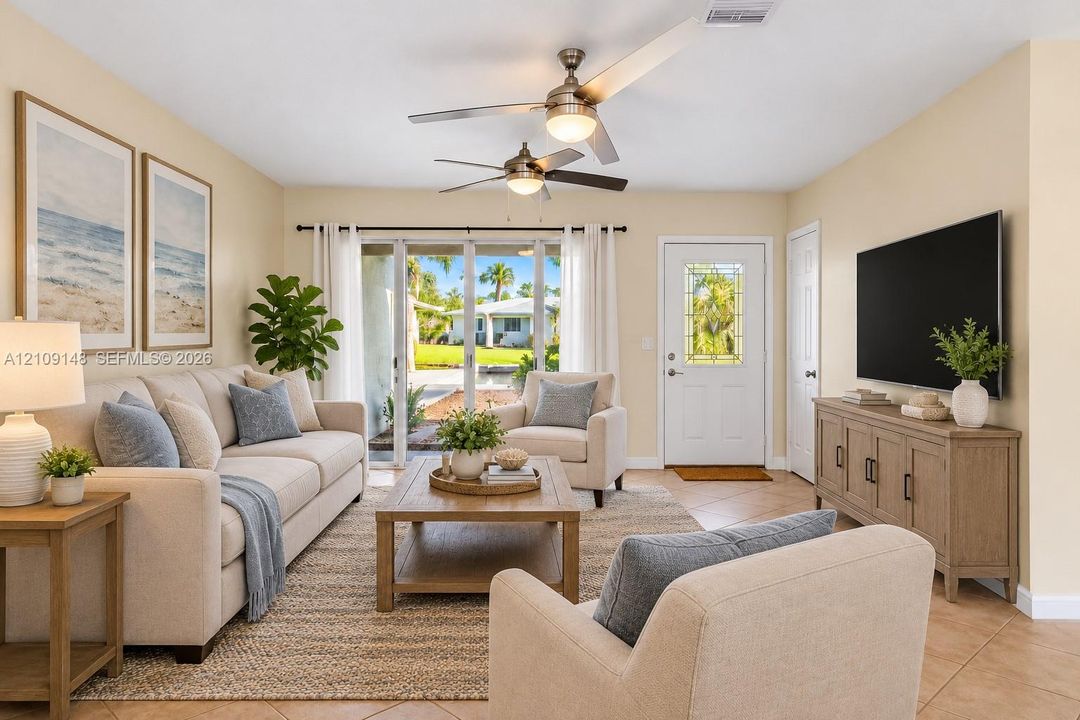 Living space featuring tile flooring, dual ceiling fans with integrated lighting, and multi-panel sliding glass doors providing outdoor access