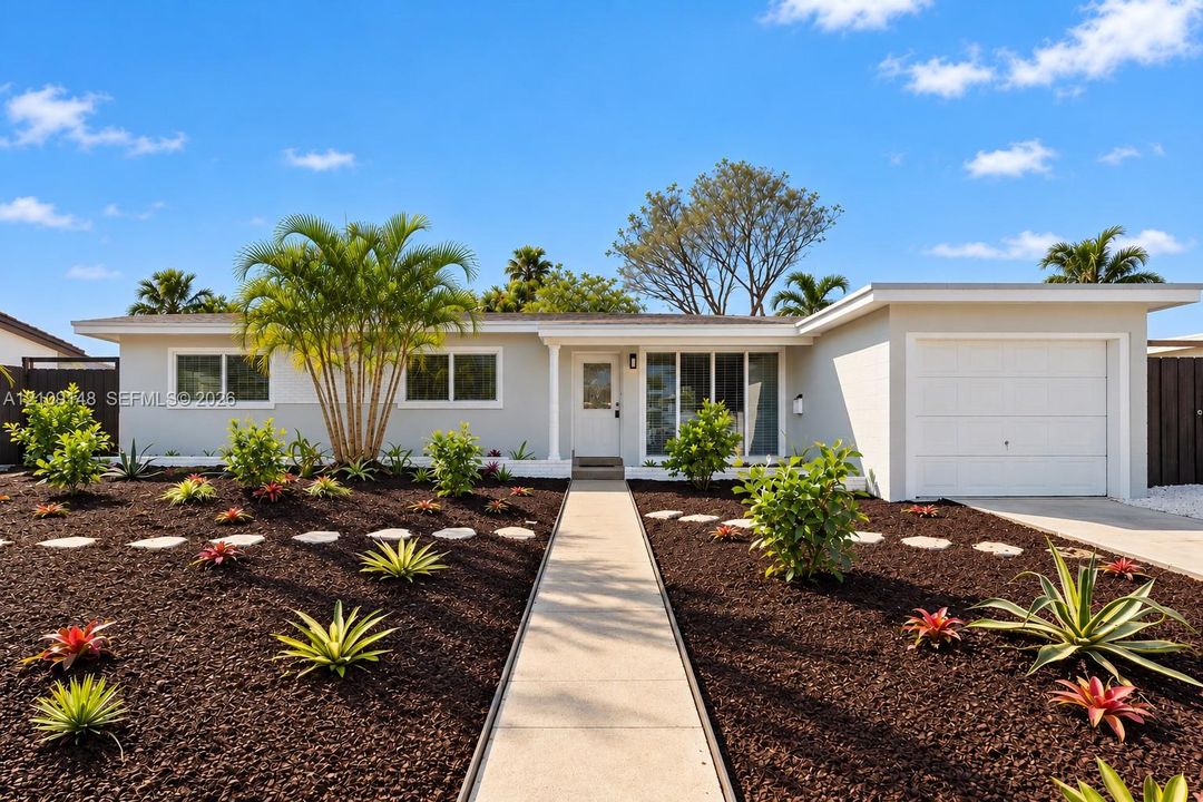 Single-story residence featuring a painted masonry exterior, attached garage, concrete walkway, and landscaped garden with stone path accents