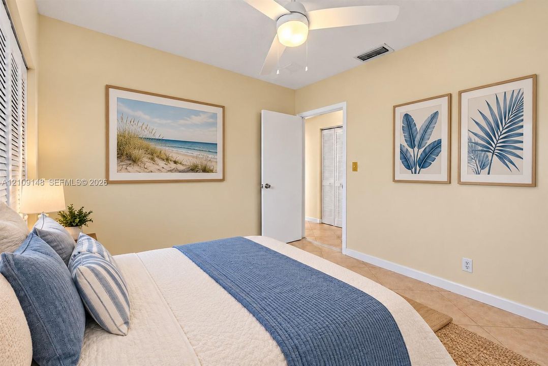 Neutral-toned interior space featuring light-colored tile flooring, a white ceiling fan with integrated lighting, plantation-style window shutters, and a closet with white louvered bi-fold doors