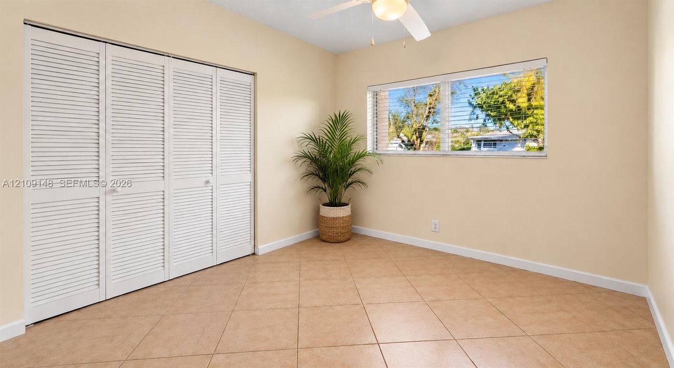 Room featuring neutral-toned tile flooring, louvered bi-fold closet doors, horizontal windows, and a ceiling-mounted light fixture