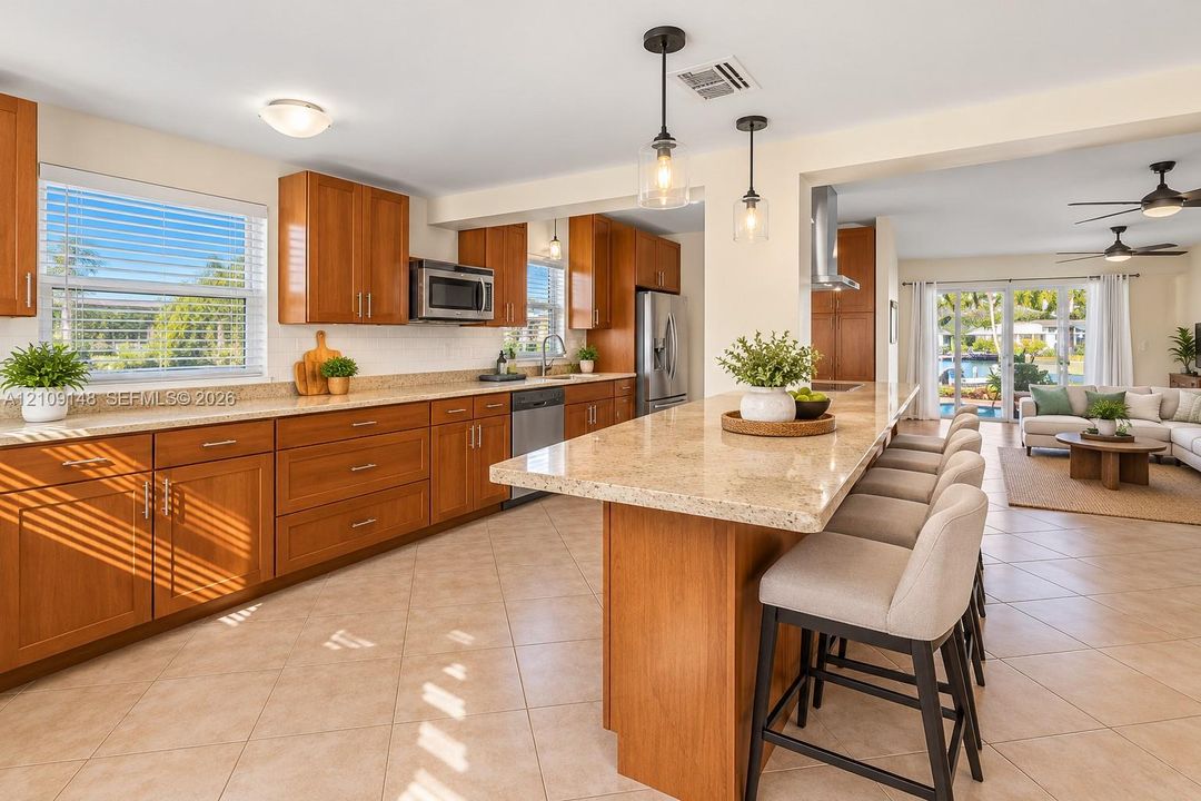 Kitchen featuring shaker-style wood cabinetry, stone countertops, a large center island with breakfast bar seating, stainless steel appliances, and tile flooring