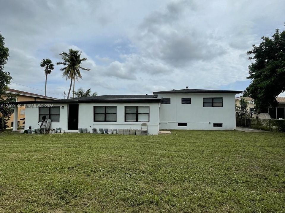 Single-story residence featuring a smooth stucco exterior, dark-trimmed window frames, a low-pitch roofline, and an expansive lawn