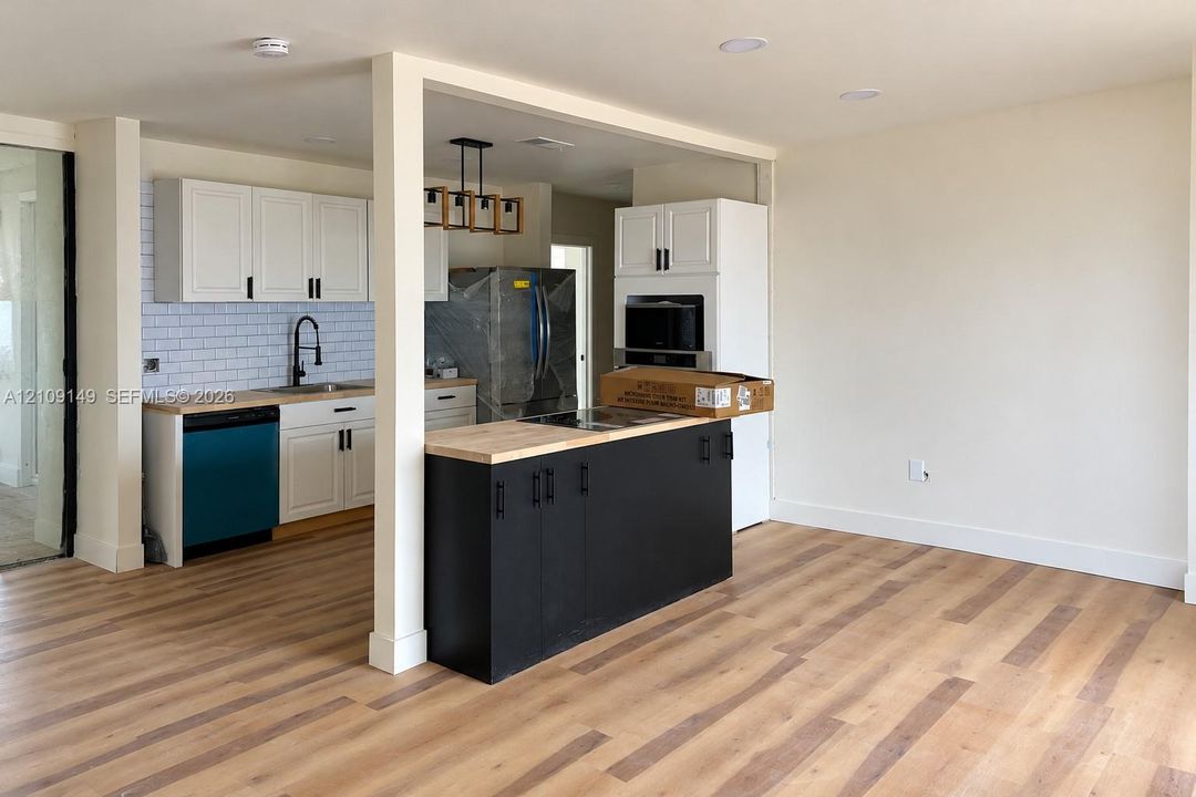 Kitchen featuring white shaker-style cabinetry, butcher block countertops, subway tile backsplash, matte black hardware, and wood-finish flooring