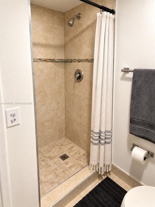 Walk-in shower featuring floor-to-ceiling tile, an integrated accent border, textured stone-style shower floor, and brushed-finish fixtures