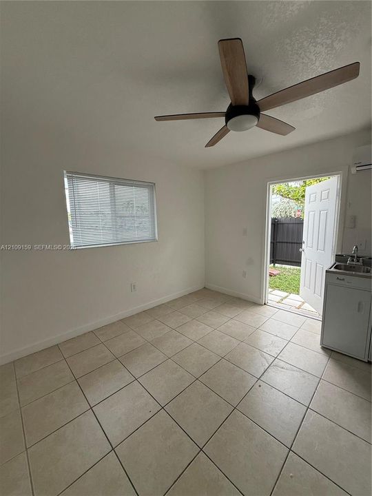 Tile flooring, ceiling fan with integrated lighting, horizontal sliding window with blinds, wall-mounted air conditioning unit, and built-in kitchenette area with sink