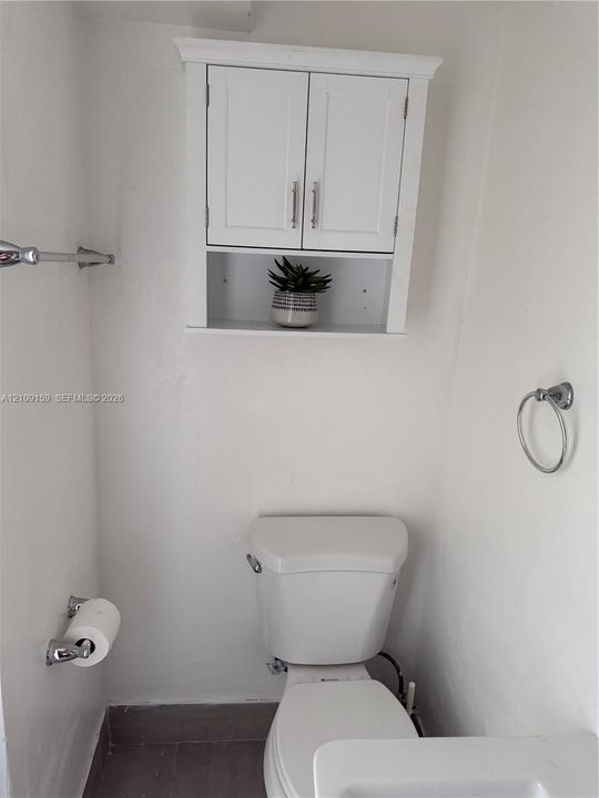 Wall-mounted white cabinetry featuring double doors and an open storage shelf, complemented by chrome hardware including a towel bar and circular ring