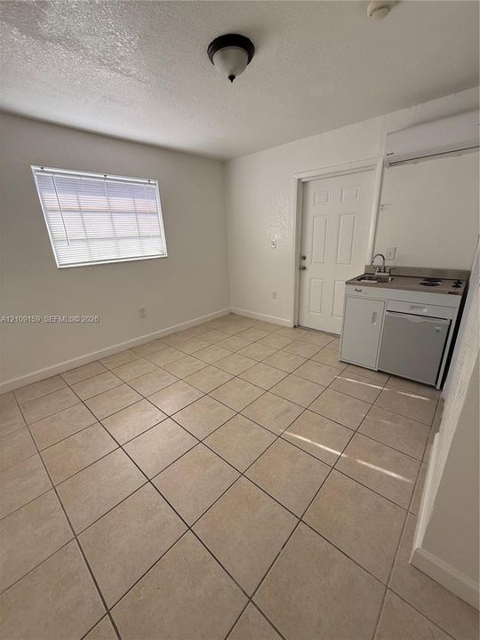 Ceramic tile flooring, white walls, and a compact kitchenette featuring a sink, two-burner cooktop, and under-counter appliance