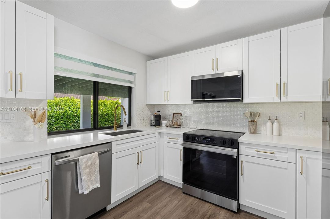 Kitchen featuring white shaker-style cabinetry, quartz countertops, a mosaic tile backsplash, wood-finish flooring, and stainless steel appliances