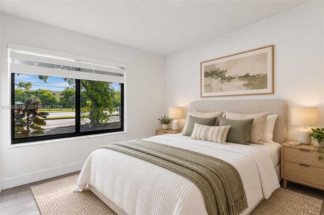 Bedroom featuring large-format window with black framing and light-toned wood-finish flooring
