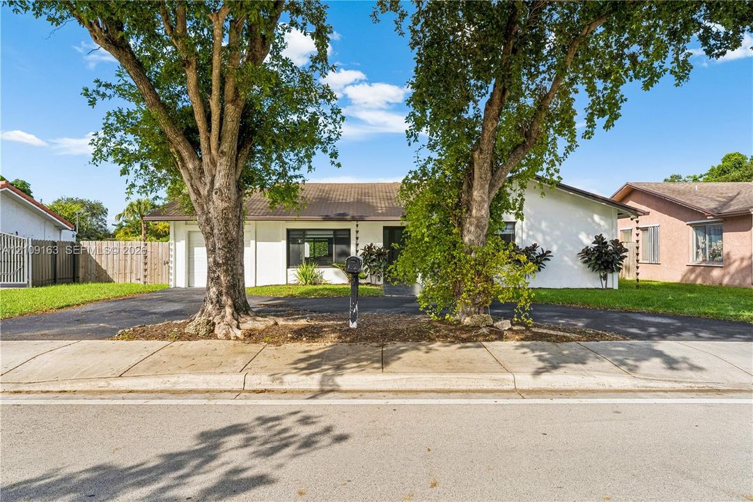 Single-story exterior featuring white stucco siding, a concrete tile roof, a paved driveway, and mature landscaping