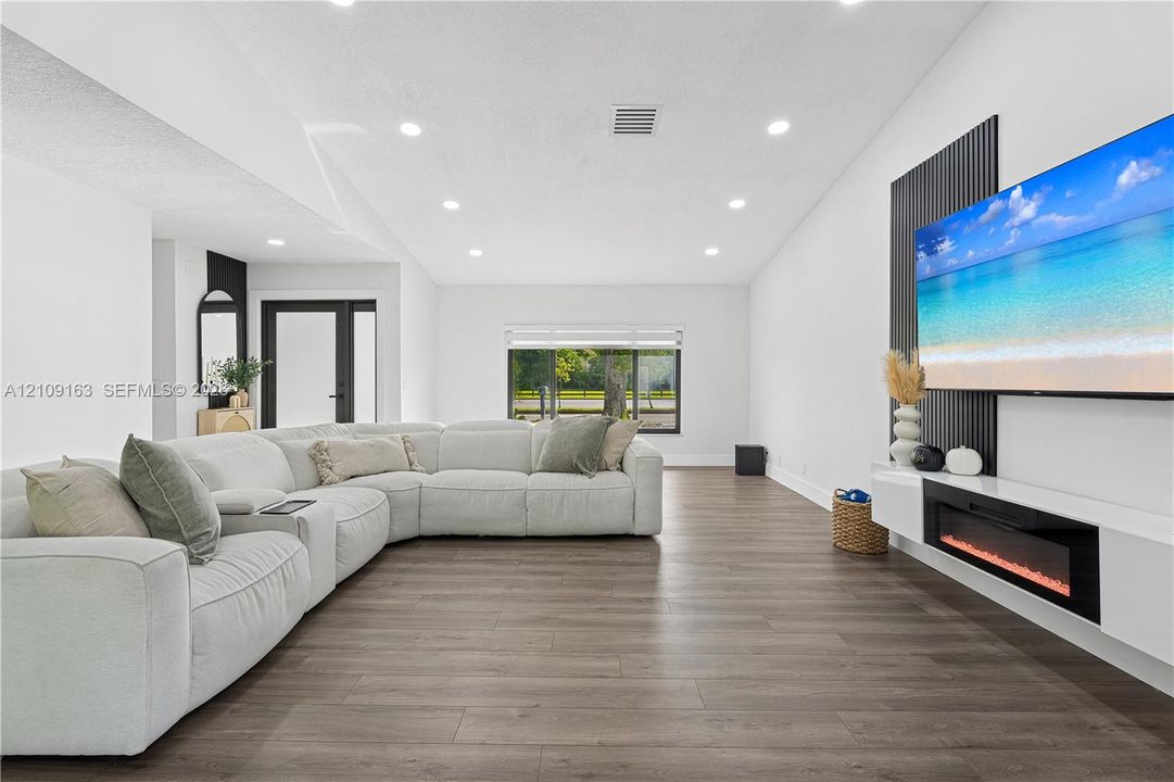 Wood-finish flooring, recessed lighting, wall-mounted linear electric fireplace, vertical slat accent wall, and glass-paneled exterior door