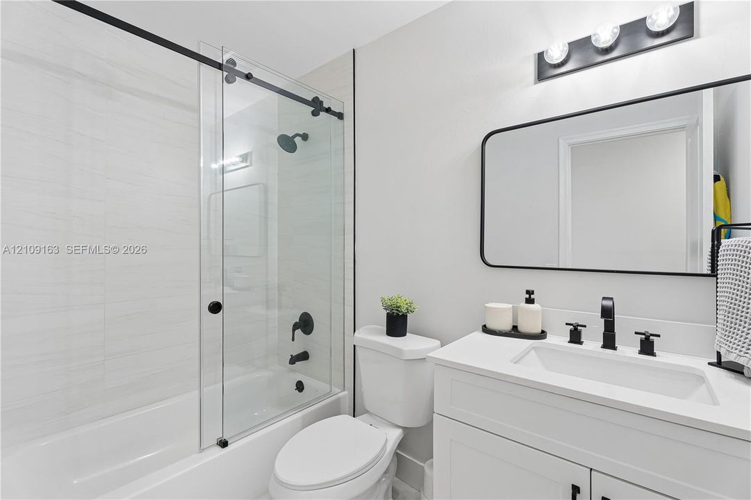 Bathroom featuring a vanity with a white countertop and rectangular undermount sink, a glass sliding shower door with matte black hardware, horizontal wall tile, and a rectangular mirror with a black frame