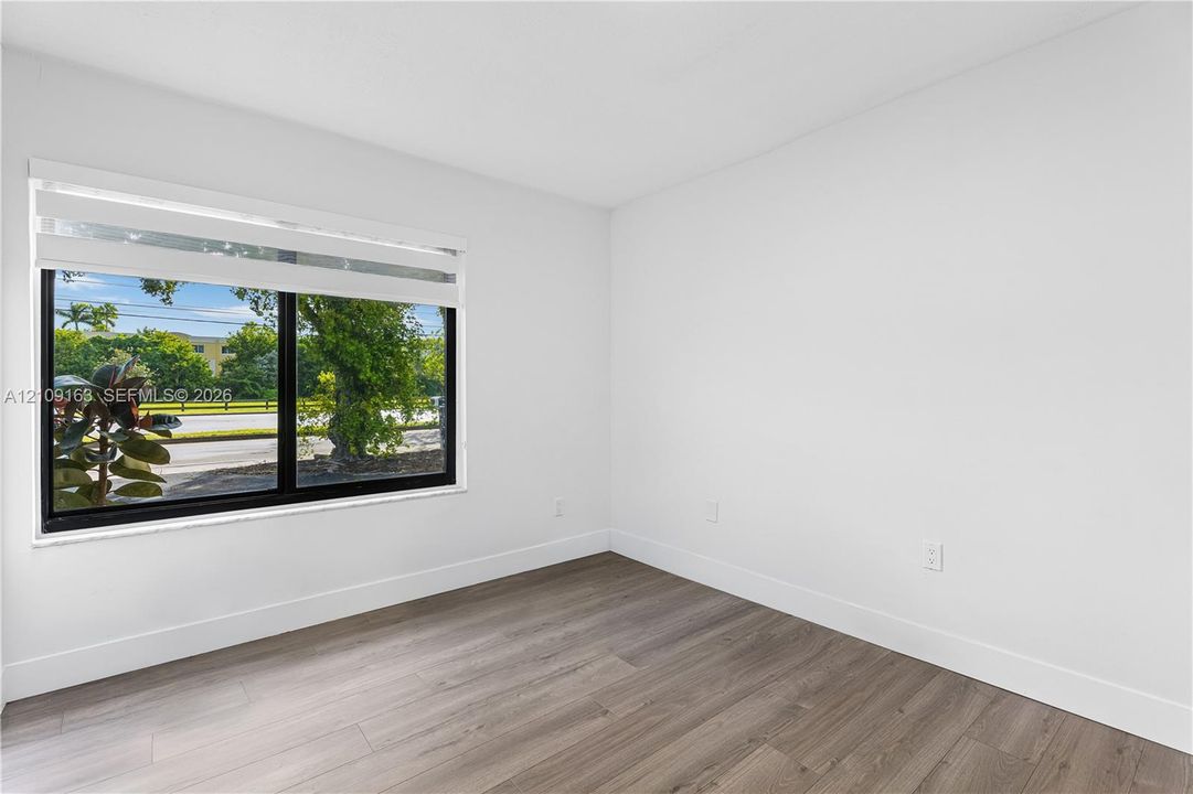 Neutral wall finishes, wood-finish flooring, and a large black-framed window with integrated blind