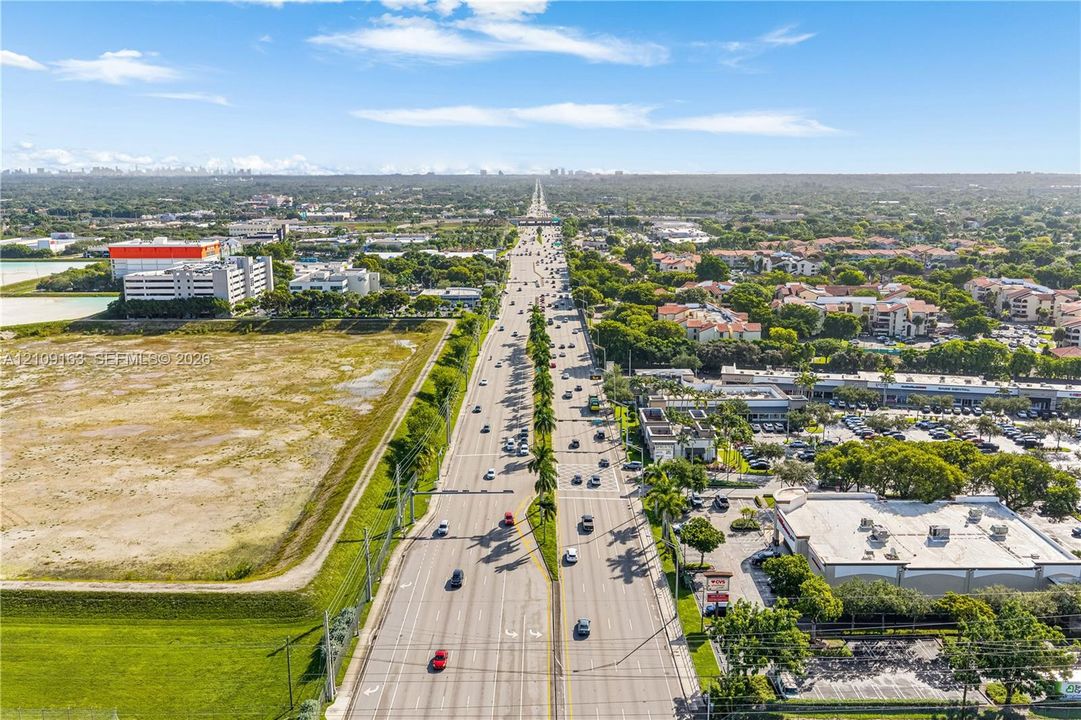 Aerial view of multi-lane thoroughfare flanked by commercial developments, surface parking lots, and open green space