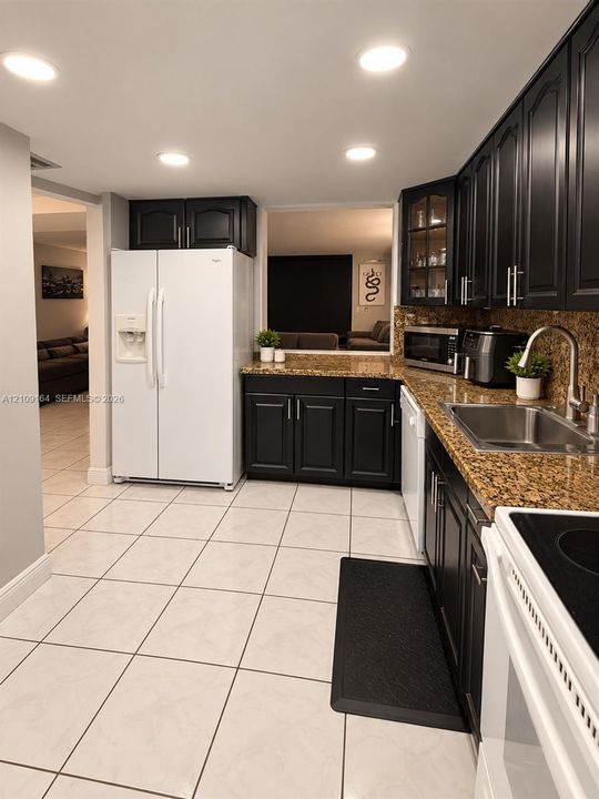 Kitchen featuring dark wood cabinetry, stone countertops, stainless steel sink with a high-arch faucet, light-toned floor tile, and recessed lighting