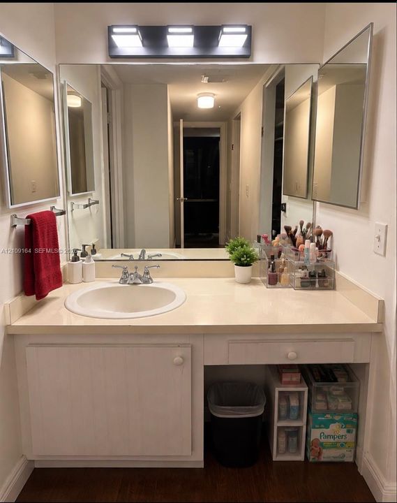 Bathroom vanity featuring a solid surface countertop with an integrated basin, brushed metal widespread faucet, large-format mirror, and three-light overhead fixture