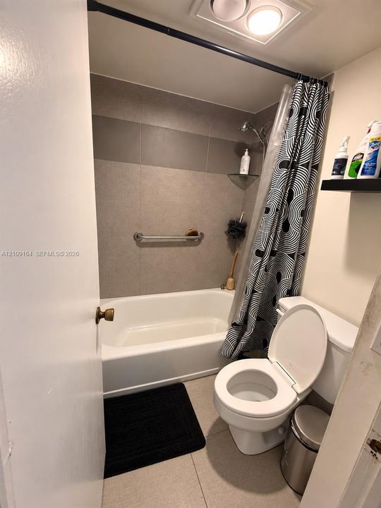 Full bathroom featuring a white bathtub with a tiled surround, a metal grab bar, a wall-mounted glass corner shelf, and a ceiling-mounted light fixture