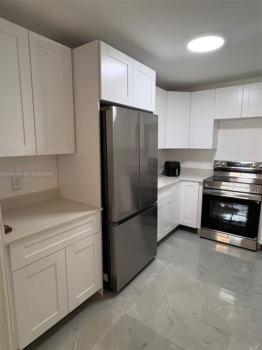 Kitchen featuring white shaker-style cabinetry, solid-surface countertops, stainless steel appliances, and tile flooring