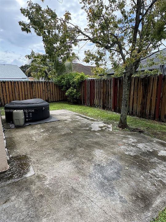 Rear exterior space featuring a concrete patio, wood privacy fencing, and a mature tree