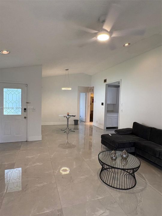 Large-format polished tile flooring, vaulted ceilings, recessed lighting, modern tiered pendant fixture, and exterior entry door with decorative glass inlay