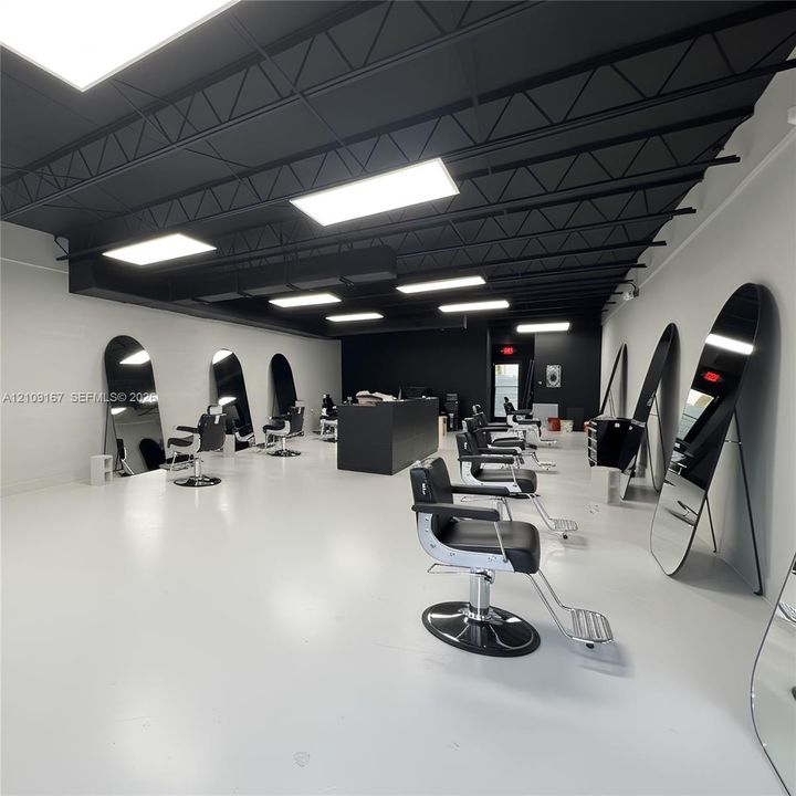 Open-concept interior featuring high-contrast black exposed ceiling trusses, bright rectangular LED panel lighting, polished light-reflective flooring, and a central matte black service counter