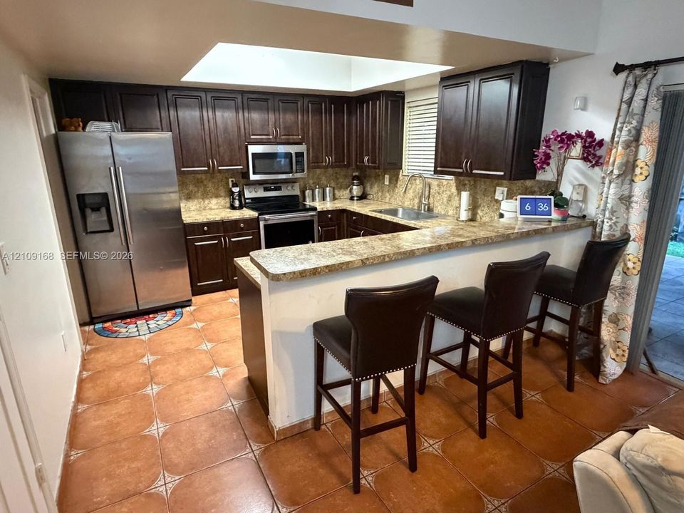 Kitchen featuring dark wood cabinetry, stone-finish countertops, stainless steel appliances, a recessed ceiling light, and ceramic tile flooring