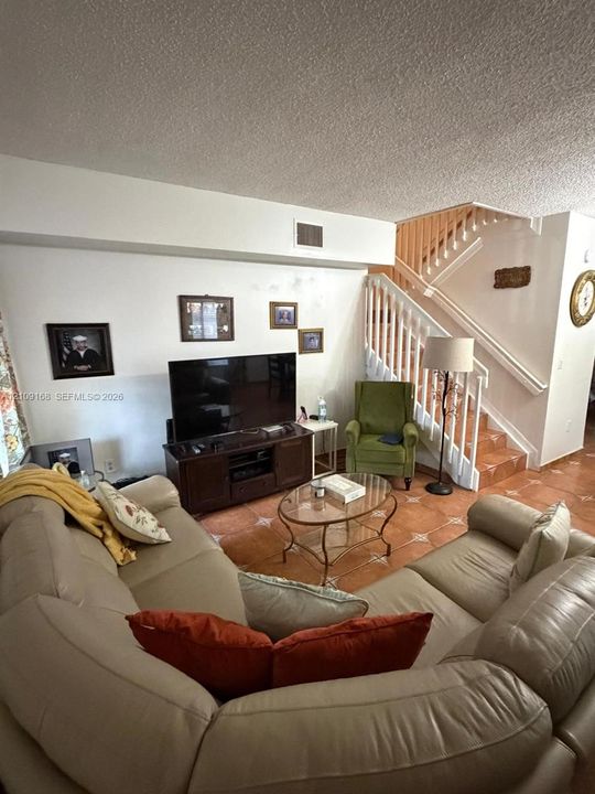 Staircase featuring white balusters, wood-finish handrails, and tile-clad steps, complemented by uniform tile flooring