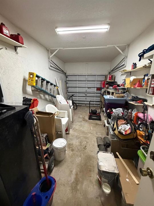 Enclosed garage featuring a metal sectional door, textured walls, concrete flooring, and ceiling-mounted fluorescent lighting