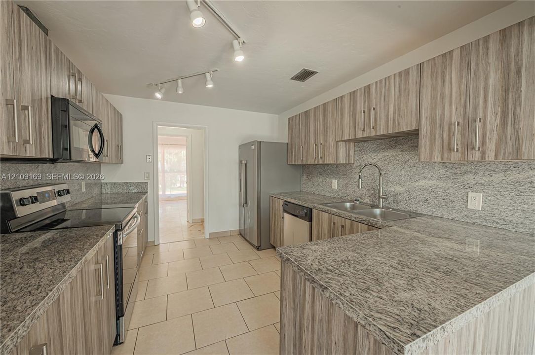 Kitchen featuring textured wood-finish cabinetry, stone countertops, stone backsplash, stainless steel appliances, and tile flooring