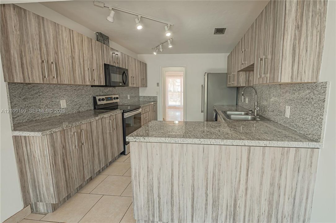 Kitchen featuring wood-grain cabinetry, stone countertops, tiled flooring, track lighting, and stainless steel appliances