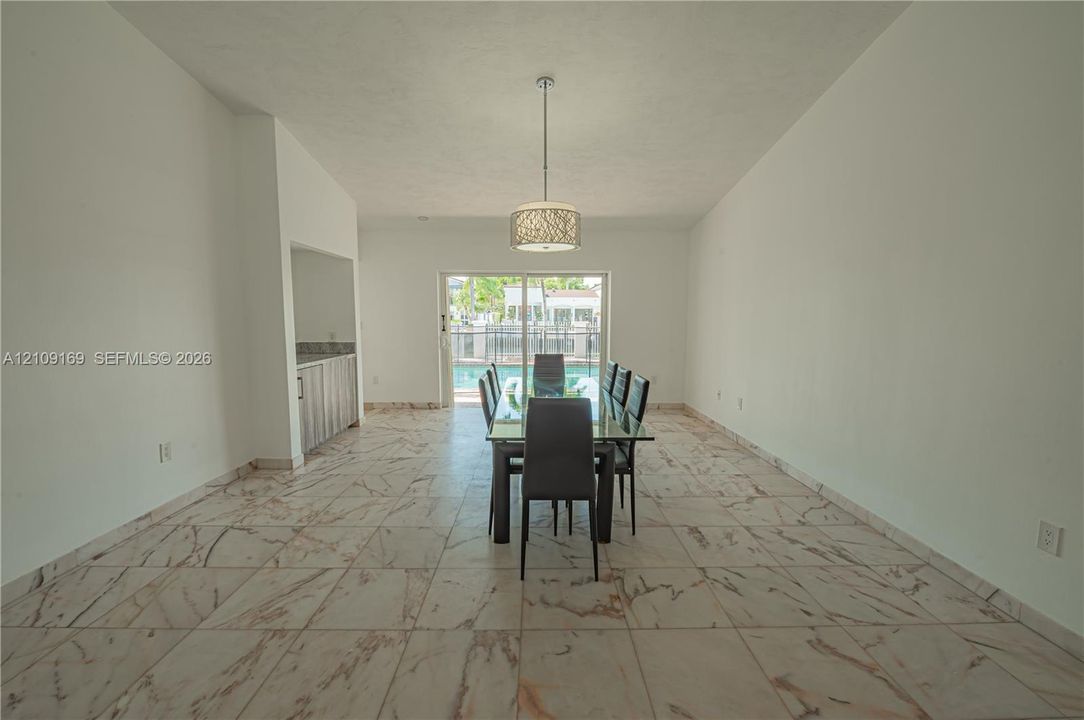 Vaulted ceilings, large-format tile flooring with veined detail, built-in wet bar, cylindrical pendant light fixture, and sliding glass doors opening to an outdoor area