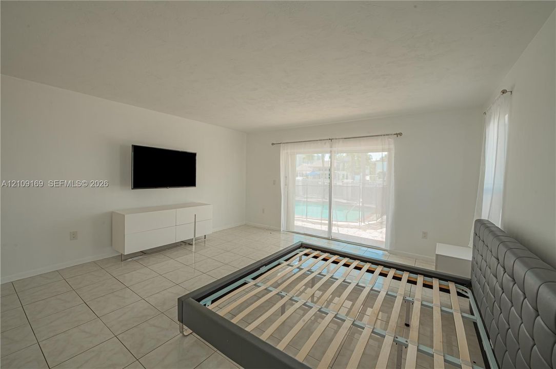 Neutral-toned tile flooring, white walls, and glass sliding doors featuring exterior access to a fenced swimming pool