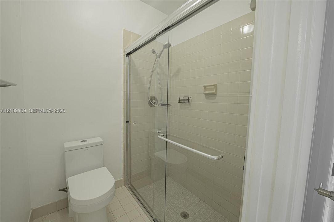 Walk-in shower featuring a sliding glass enclosure, ceramic tile surround, integrated shower bench, and a handheld shower fixture, paired with a dual-flush toilet