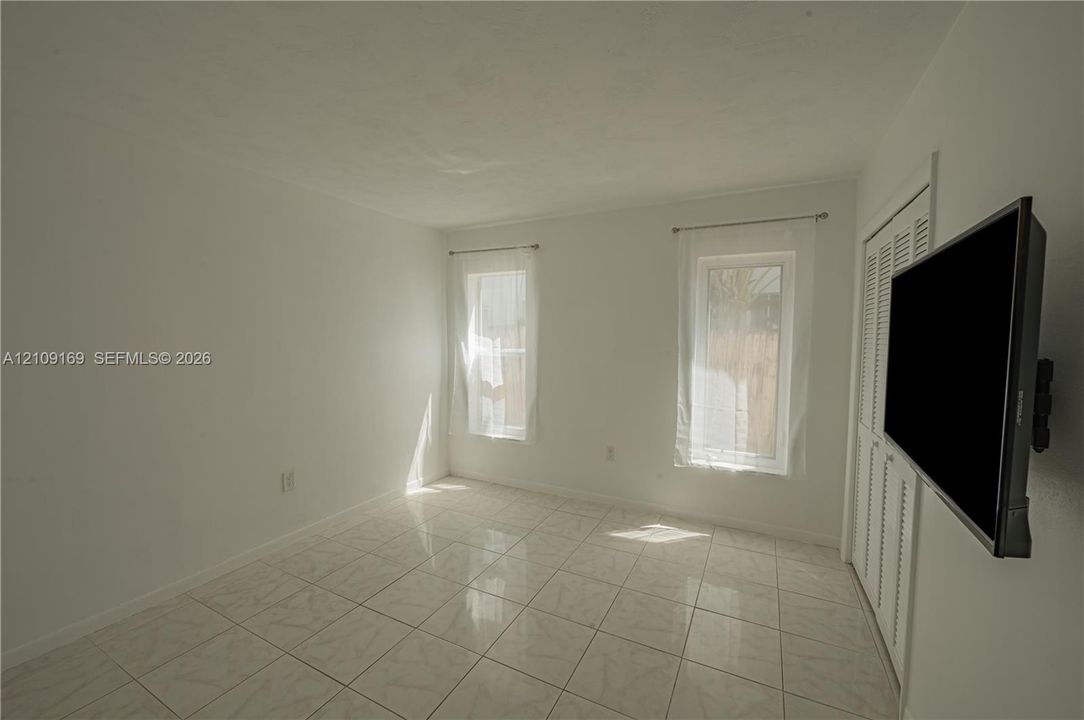 Neutral-toned tile flooring, dual windows with natural light, and louvered bifold closet doors