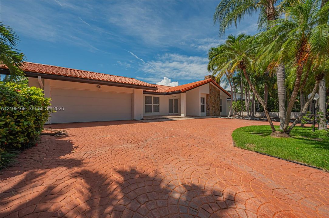 Single-story residence featuring a tile roof, decorative stone chimney exterior, spacious stamped concrete driveway, and established palm trees