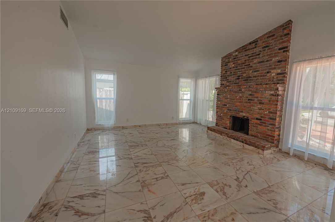 Vaulted ceiling, floor-to-ceiling brick fireplace with a raised hearth, and polished stone-finish tile flooring