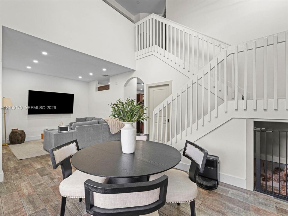 High-ceiling interior featuring a wooden staircase with vertical balusters, wood-finish flooring, recessed lighting, and an arched doorway