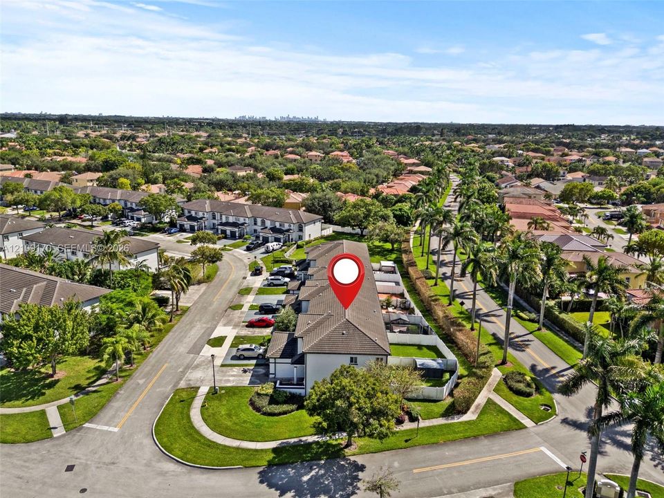 Aerial view of a multi-unit residential building featuring a tile roof, concrete driveway, and enclosed backyard space situated within a landscaped neighborhood