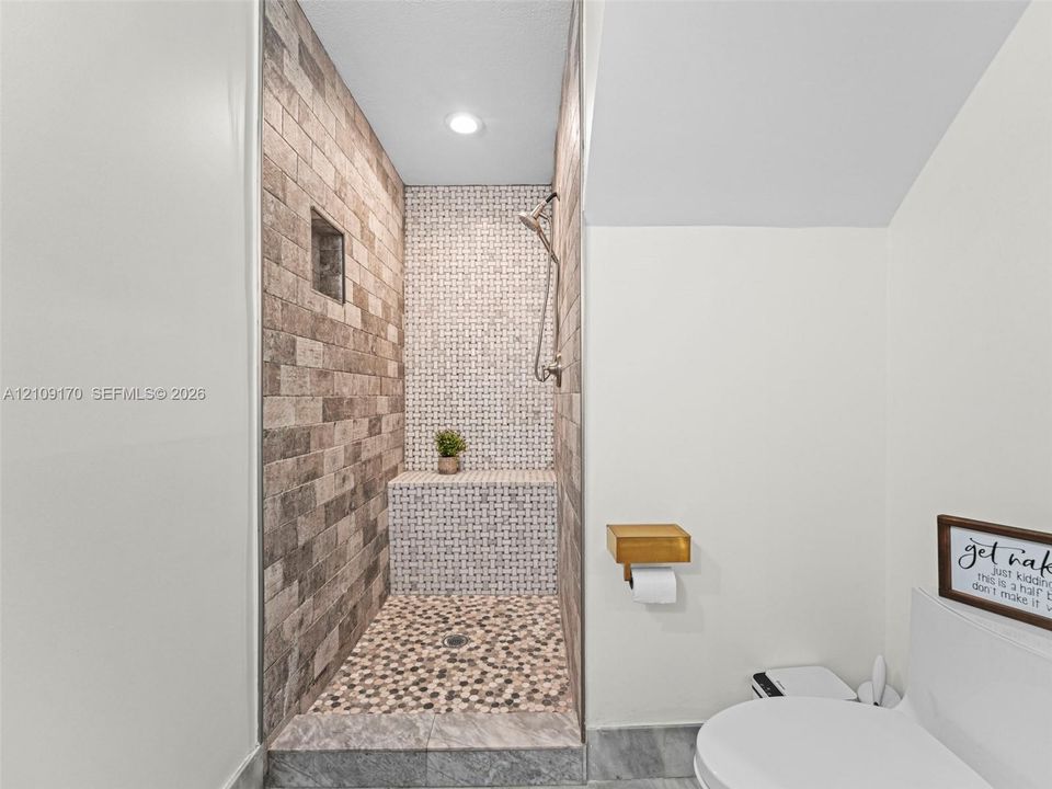 Walk-in shower featuring a brick-style tiled wall, mosaic-tile accents, built-in tiled bench, river-stone flooring, and a metal shower fixture