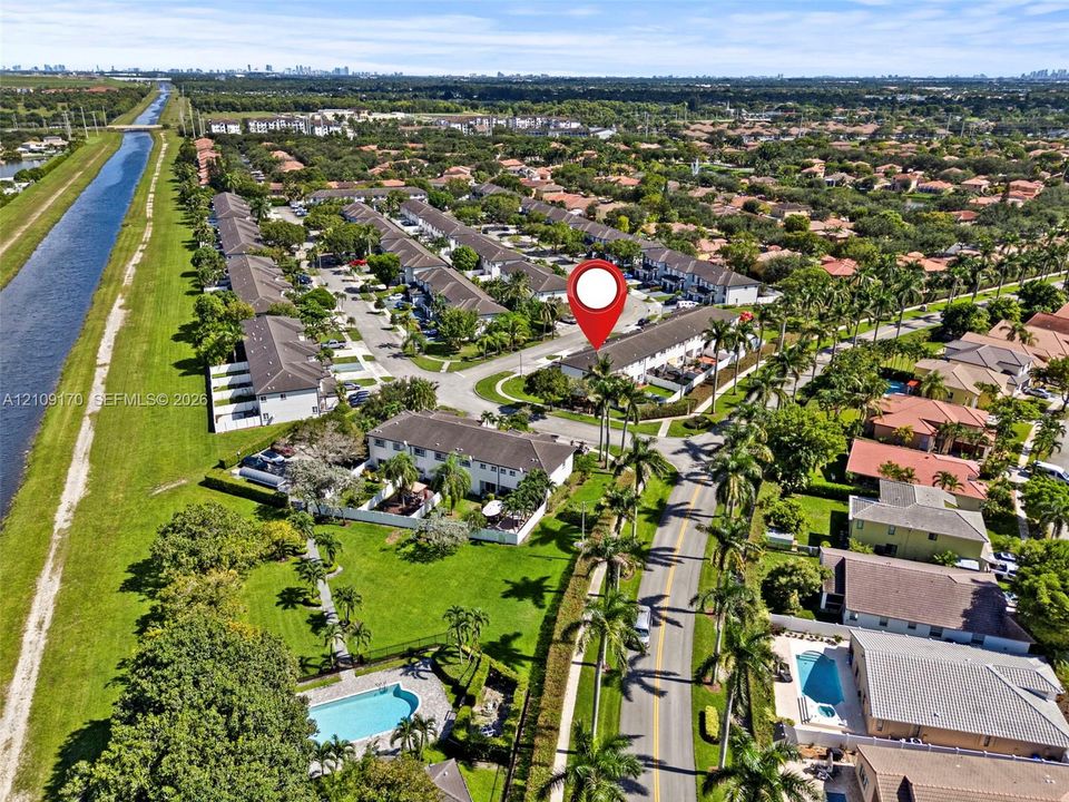 Aerial perspective of a multi-unit residential community featuring manicured landscaping, palm trees, and an open-air swimming pool