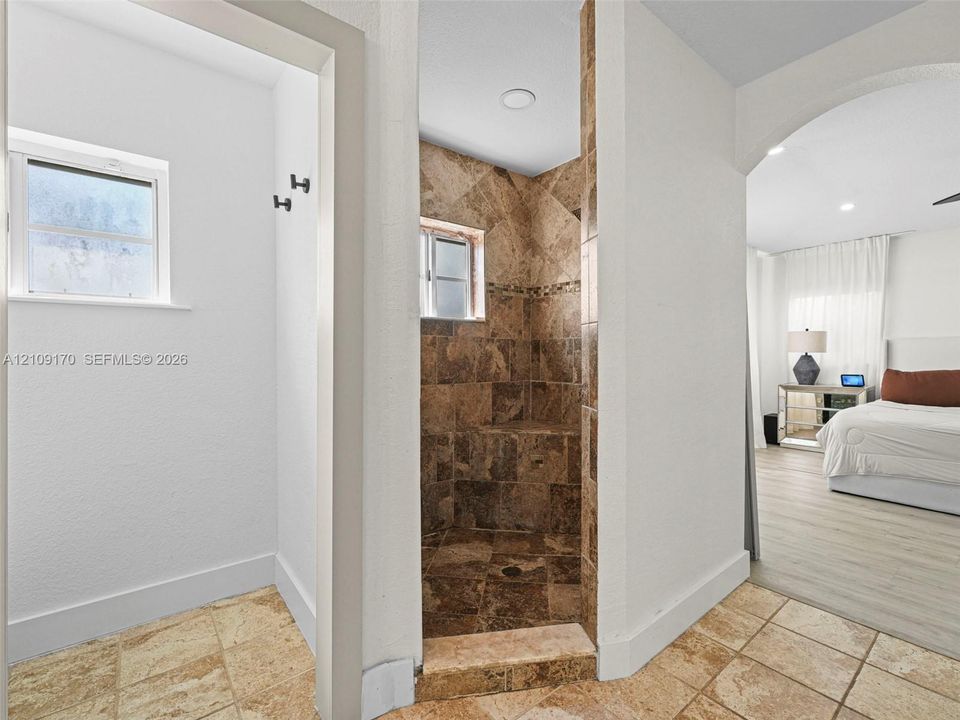 Walk-in shower featuring brown stone-style tile surround and floor, built-in tiled bench, recessed lighting, and stone-style flooring