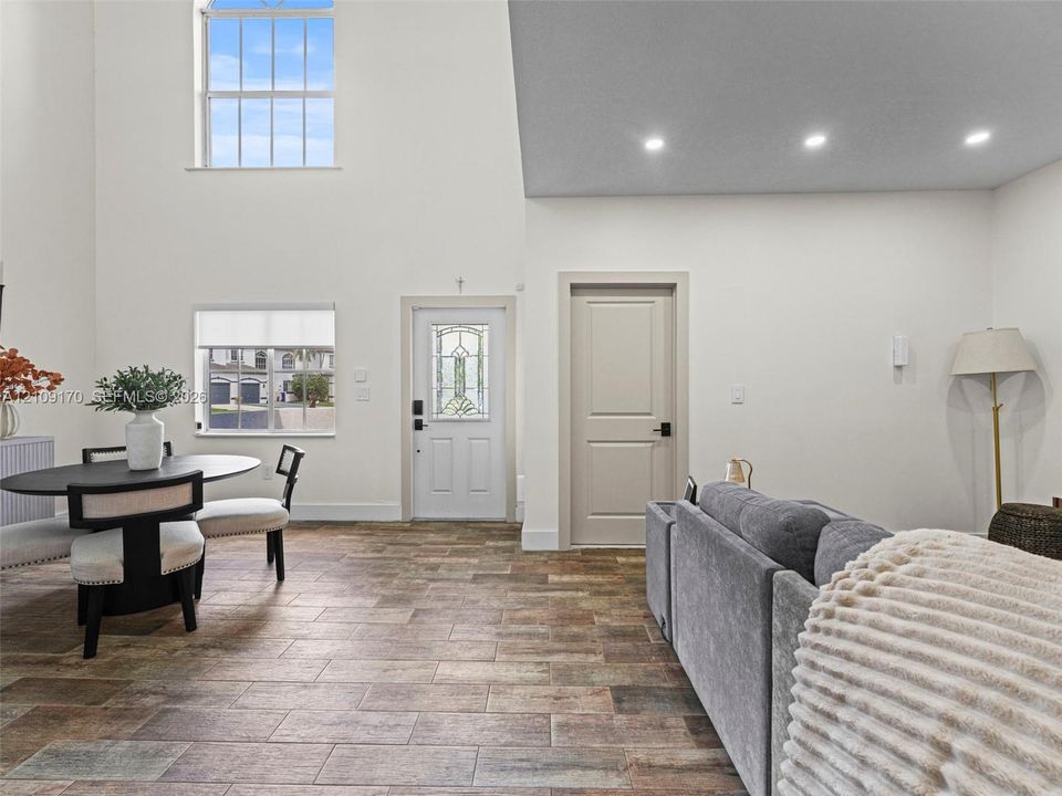 High-ceiling interior space featuring multi-tonal rectangular tile flooring, recessed lighting, double-hung windows, and a glass-inset entry door