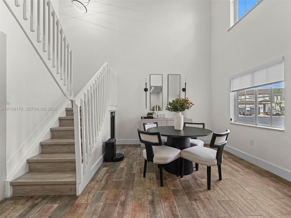Double-height ceiling, staircase with white wood balusters, wood-finish flooring, and multi-pane windows